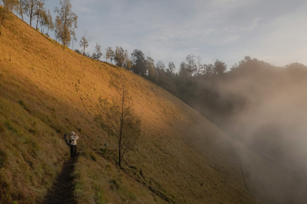Older man stretching on a hillside trail at sunrise