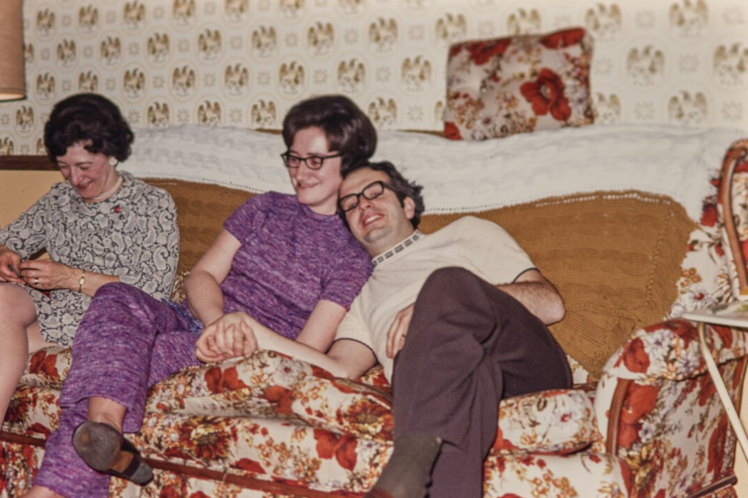 Small group of older adults conversing on sofas with cups of tea