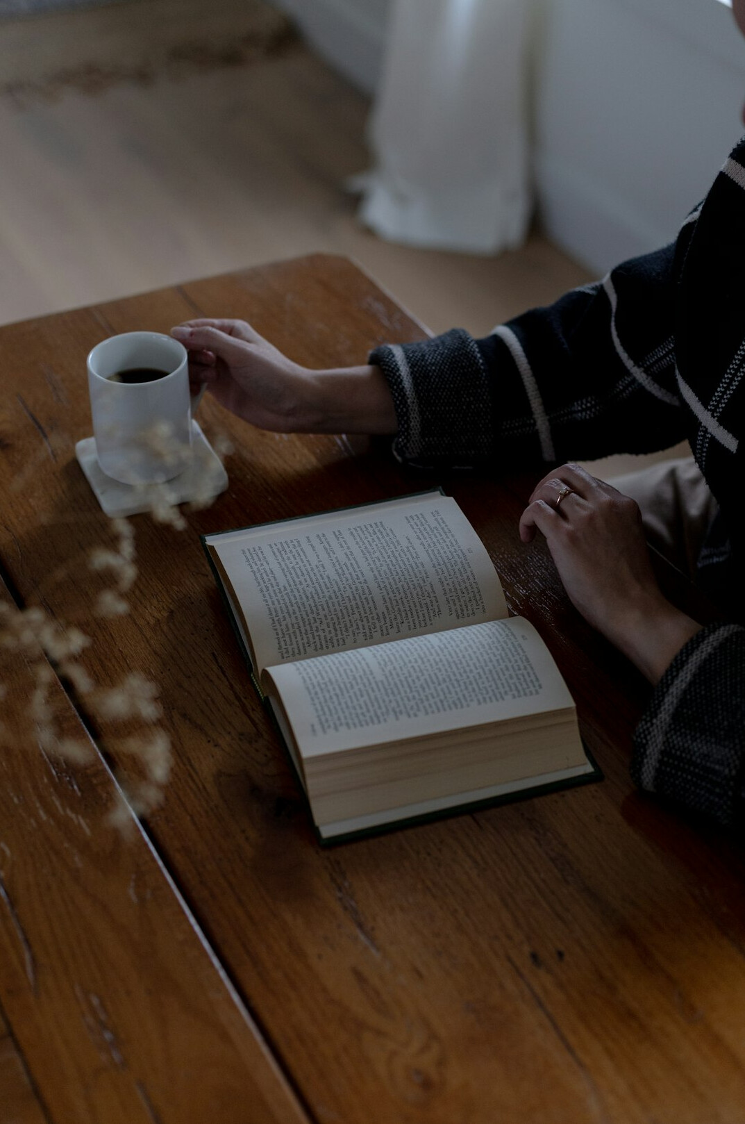 Close-up of an older person's hands holding a steaming cup of tea beside an open notebook